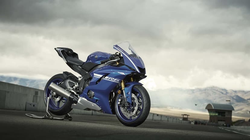 Blue Yamaha YZF-R6 sportbike on a rear stand at a racetrack with mountains and a cloudy sky background.