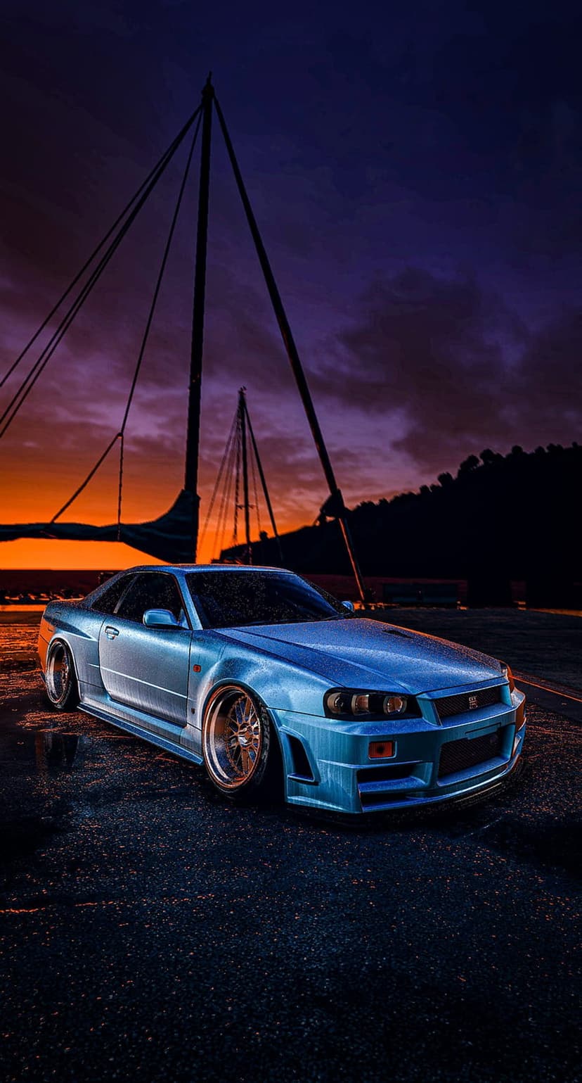 Nissan Skyline R34 GTR in blue parked on wet ground with a sailboat silhouette against a purple and orange sunset.