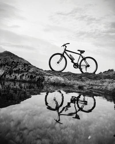 Monochrome Bicycle Reflection on Rocky Shore Mobile Wallpaper