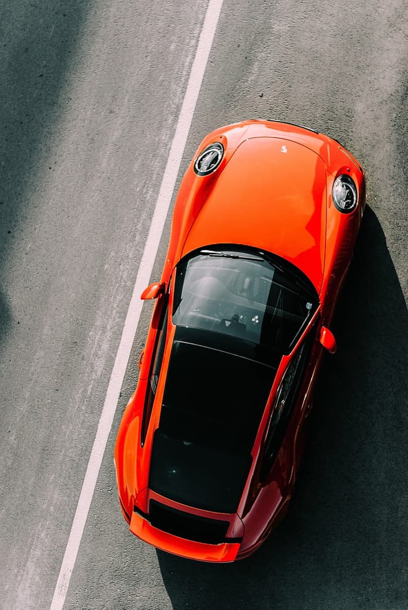 Red sports car parked on dark textured asphalt with a white lane stripe seen from a direct overhead perspective.