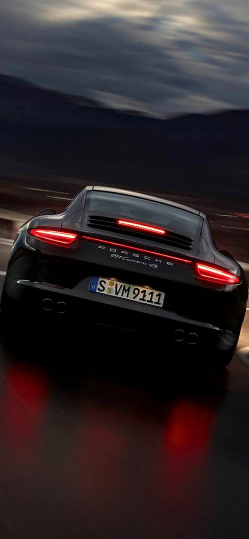 Rear of a black Porsche 911 Carrera 4S at night with glowing red taillights and motion blur on a dark road.