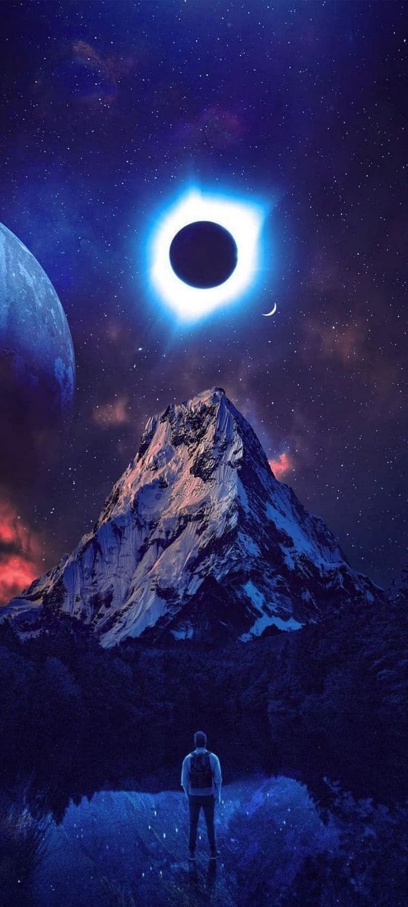 Blue solar eclipse glows above a snowy mountain peak and a lone person standing beside a reflective alpine lake.