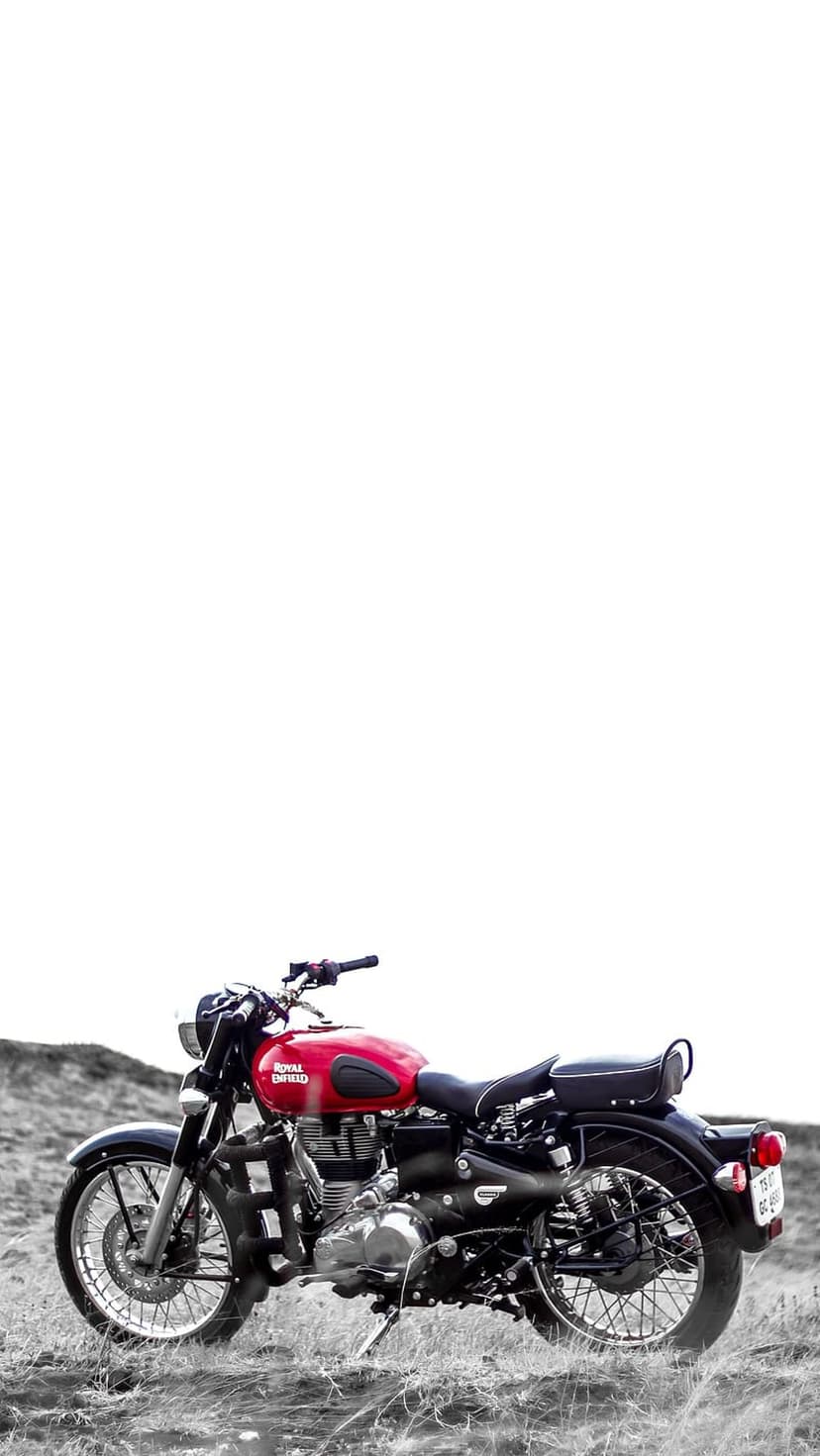 Red Royal Enfield Classic 350 motorcycle parked on a grayscale grassy hill against a bright white sky backdrop.