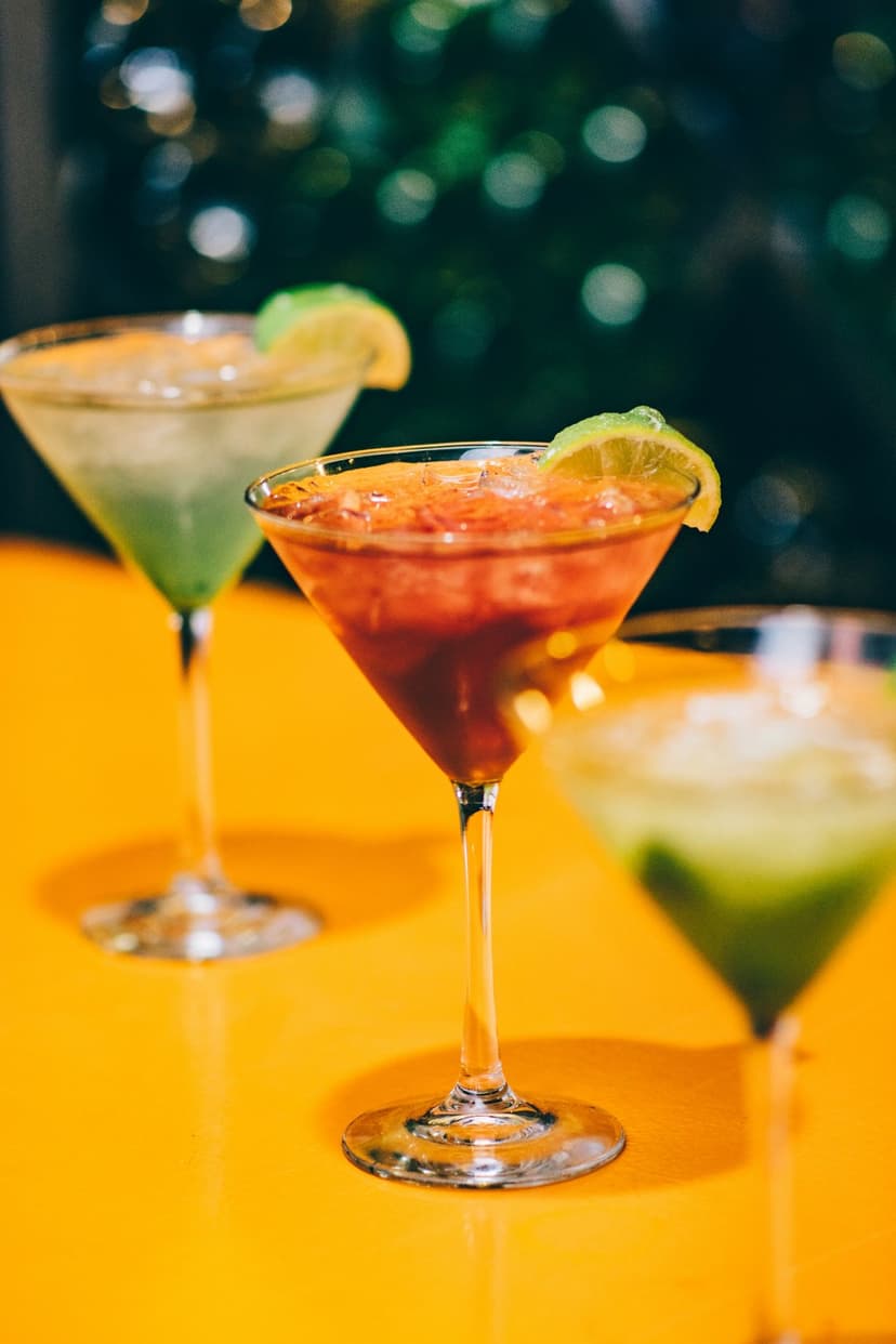 Three martini glasses with lime slices on an orange table against a blurred green bokeh background.