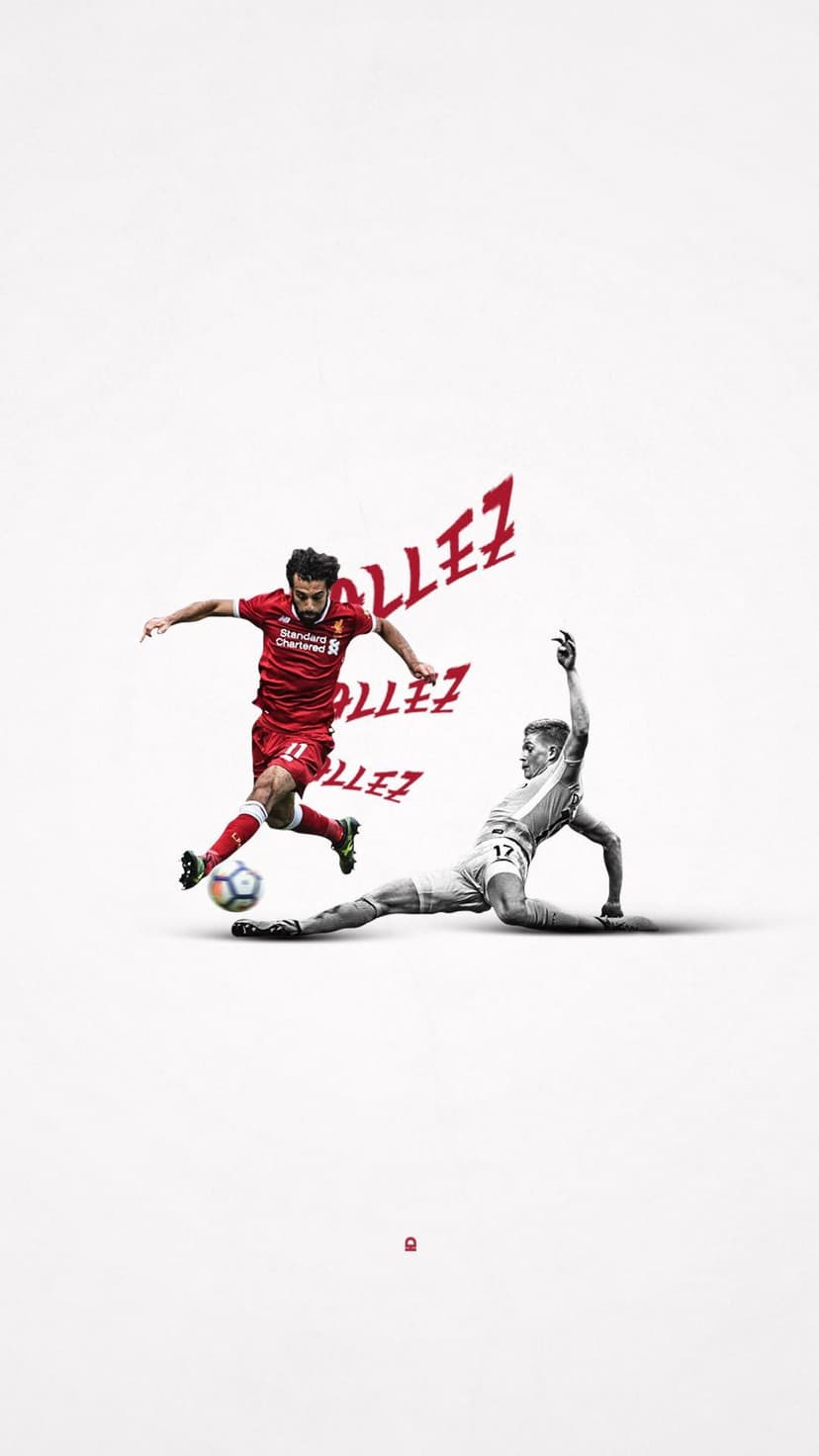 Mohamed Salah in a red Liverpool kit prepares to kick a soccer ball while a defender slides to block him.