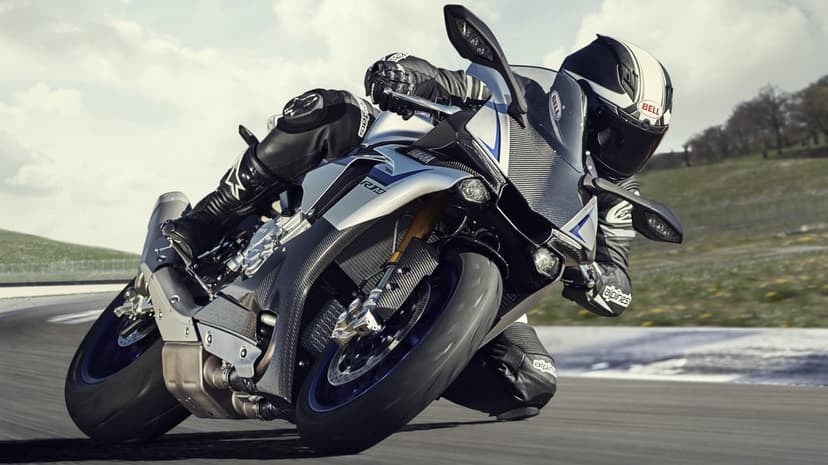 Yamaha R1M sportbike leaning deep into a racetrack corner with a rider in black and white leather gear.