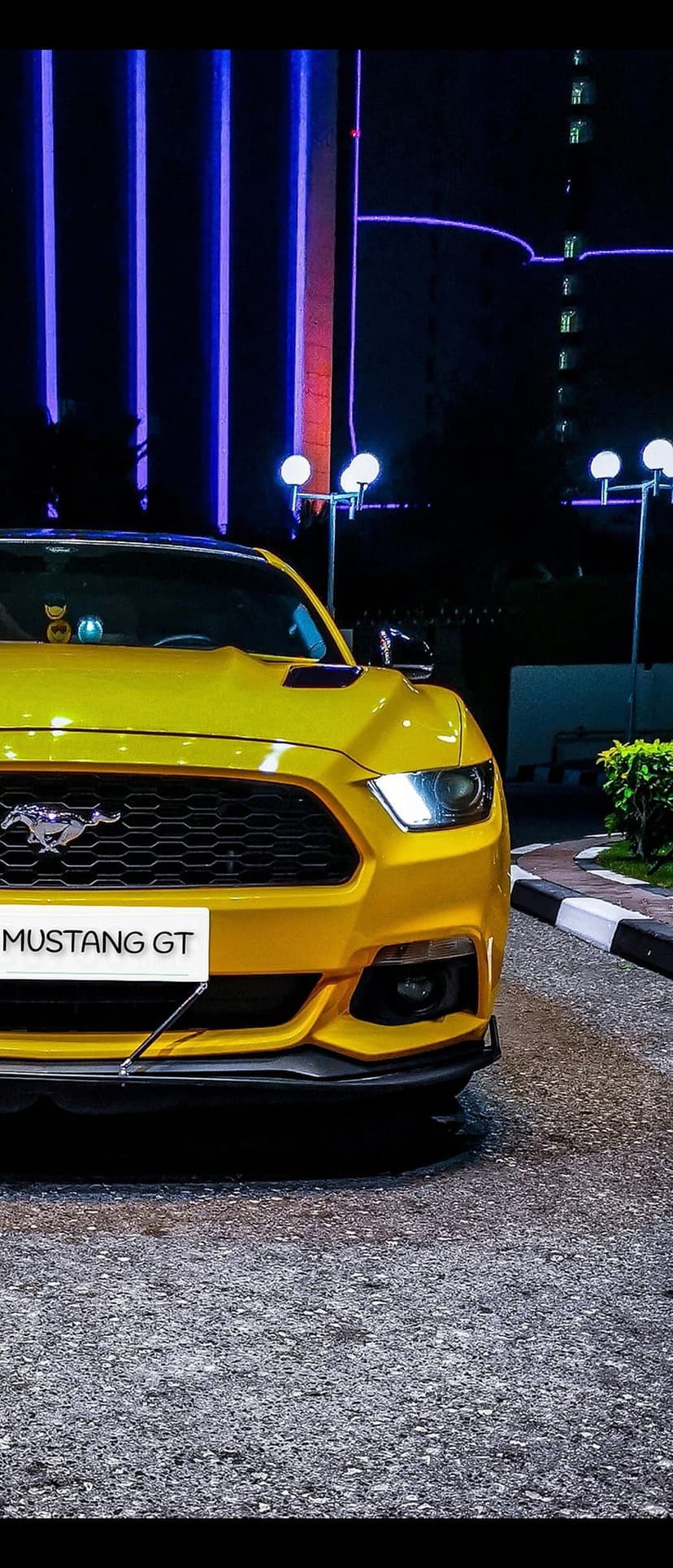 Yellow Ford Mustang GT parked at night on an asphalt road with vertical purple neon lights in the background.