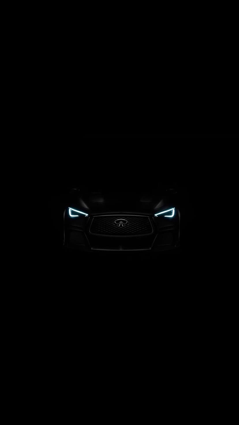 Infiniti car with illuminated LED headlights and a dark metallic finish positioned in a low-light studio setting.