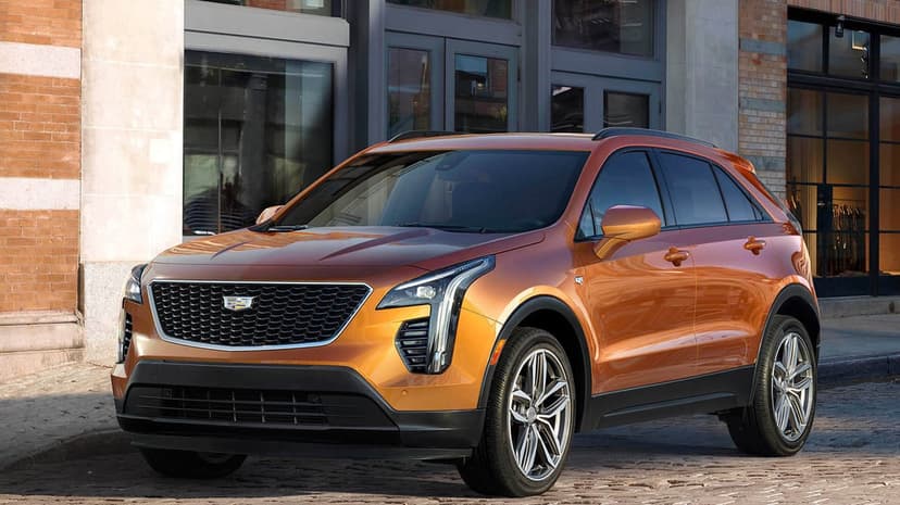 Metallic orange Cadillac XT4 parked on a cobblestone street with a brick building and glass windows.