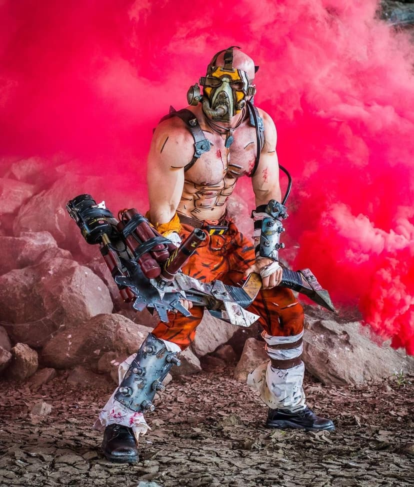 Muscular man in a psycho mask holding a buzz axe weapon amidst thick red smoke and rocky terrain.