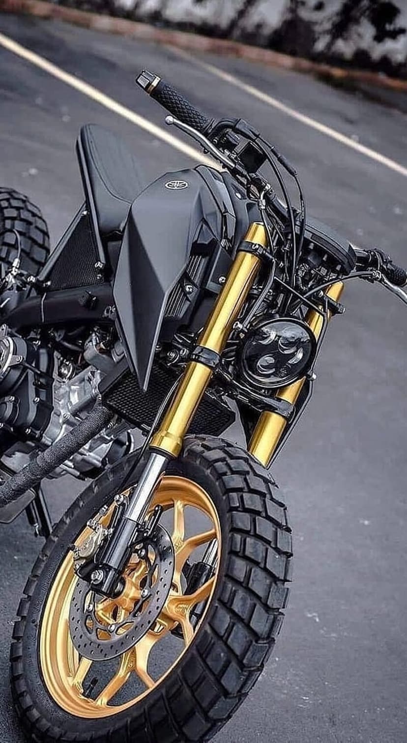 Black custom motorcycle front end with golden forks, an LED headlamp, and a gold spoke wheel with knobby tire.