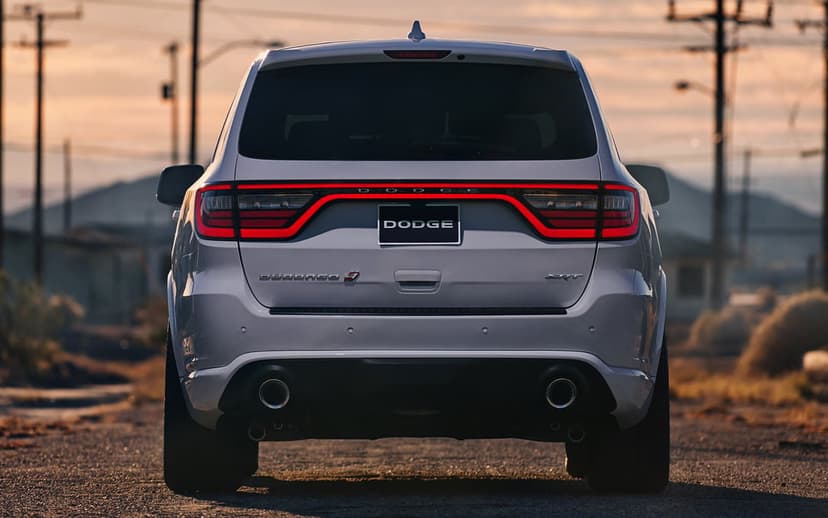 Rear view of a silver Dodge Durango SRT with glowing red LED taillights on a road at sunset.