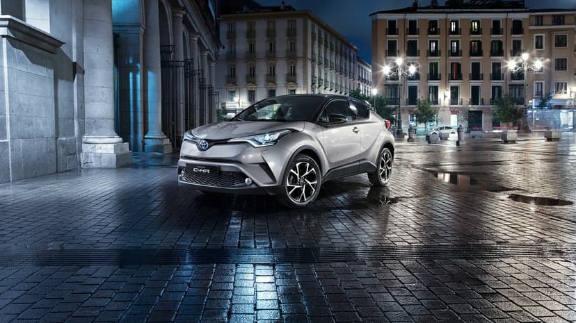 Silver Toyota C-HR SUV on wet city cobblestones at night with reflections and urban architecture.