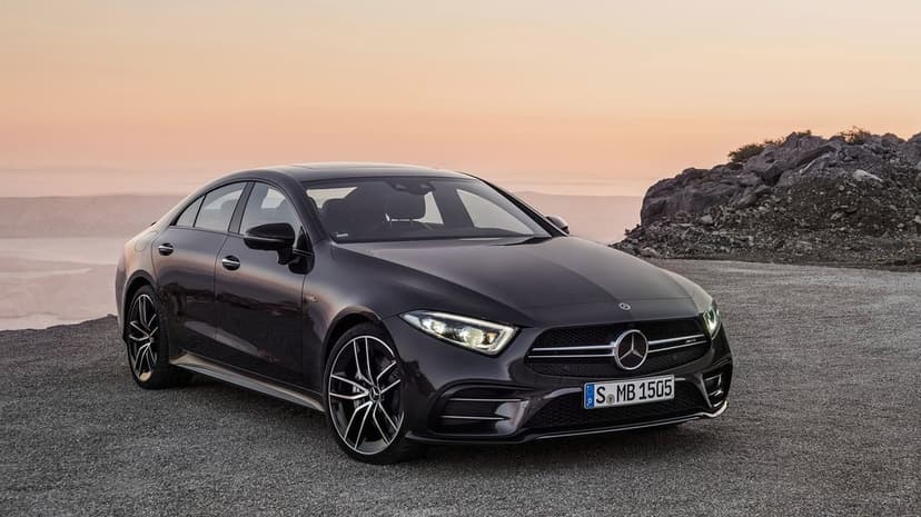 Dark Mercedes-Benz AMG parked on a gravel cliffside road against a soft pink and orange sunset sky.