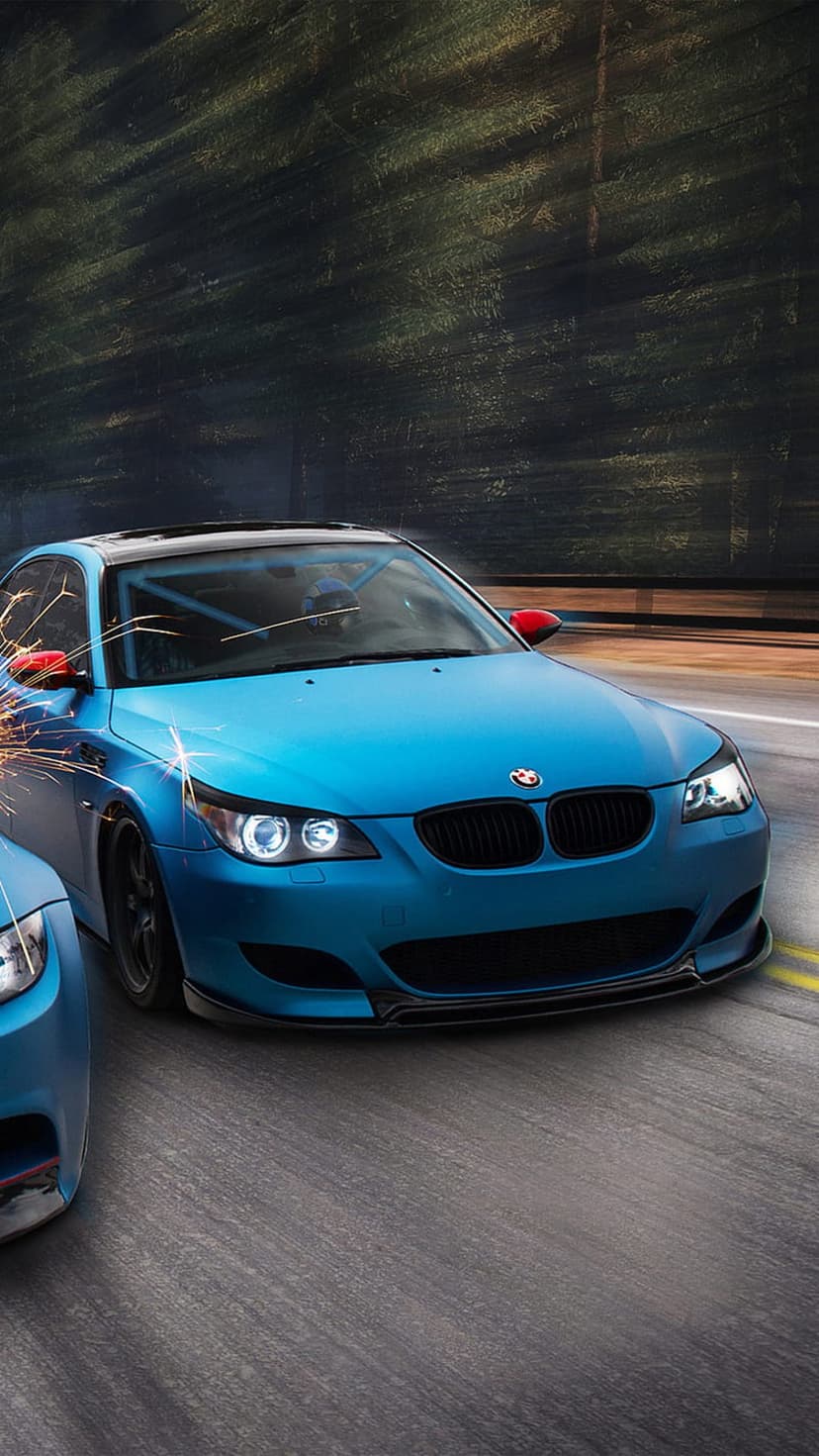 Blue BMW M5 sports cars drift on a forest road with sparks flying from the chassis and visible red side mirrors.