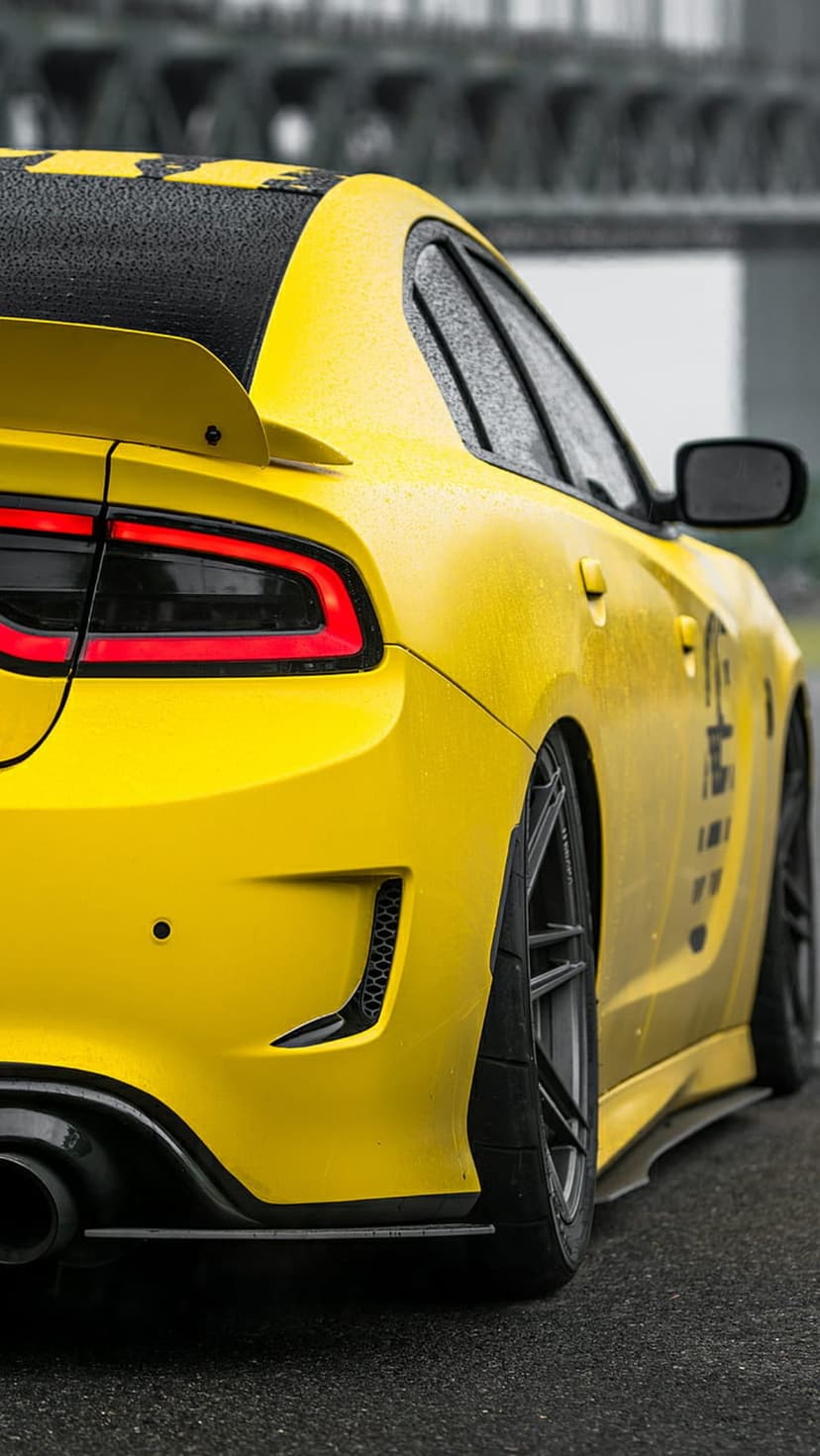 Yellow Dodge Charger with a black spoiler and diffuser features water droplets on glossy paint in the rain.