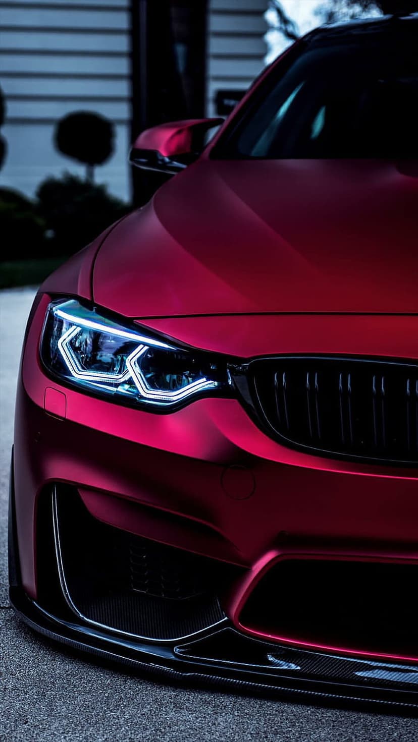 BMW M4 Coupe with matte red paint, distinctive LED angel eye headlights, and a black kidney grille on asphalt.