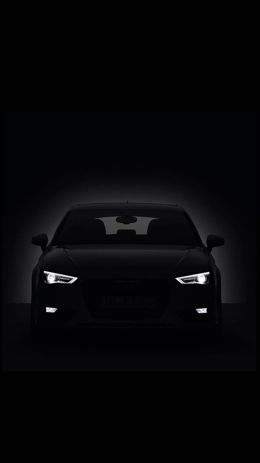 Audi sedan silhouette with glowing white LED headlights and a bat-shaped reflection on the dark windshield glass.