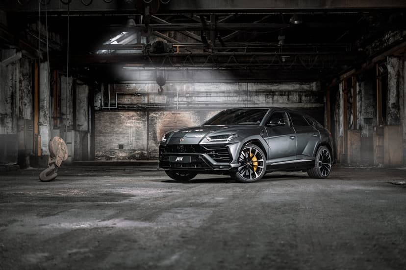 Dark grey Lamborghini Urus with yellow brake calipers parked in a moody, industrial warehouse with spotlighting.