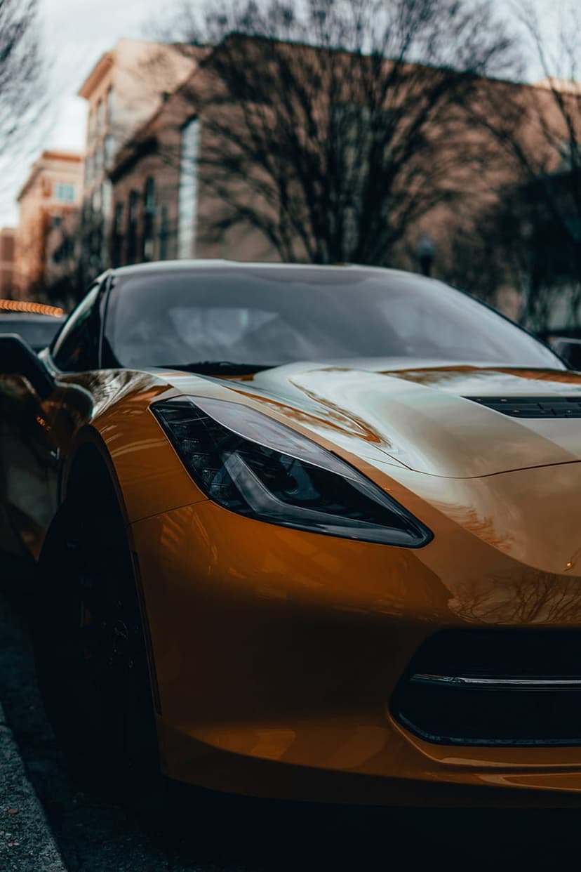 Gold Corvette C7 hood and LED headlight show metallic reflections against a blurred urban background.