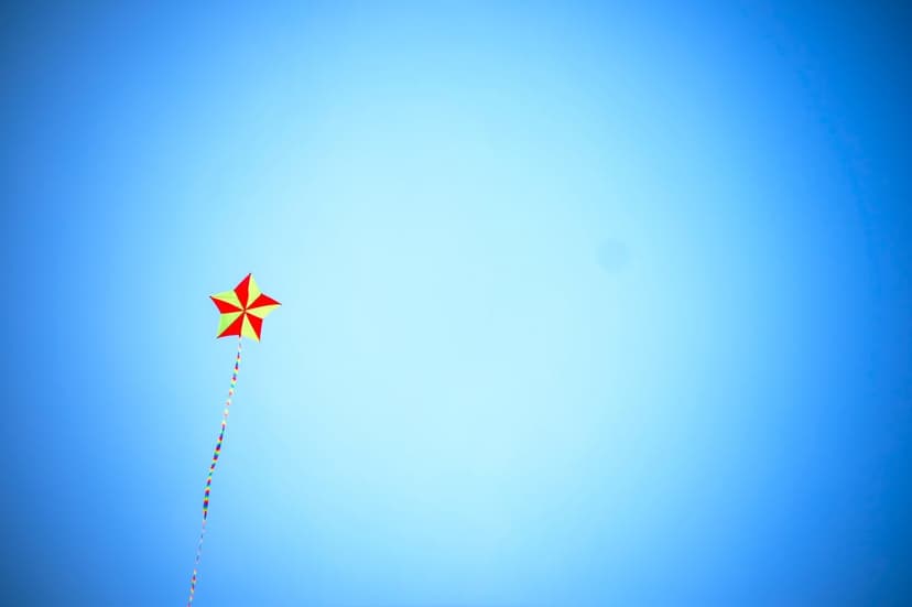 Star-shaped kite with red and yellow panels flying high in a clear blue gradient sky with a long trailing tail.