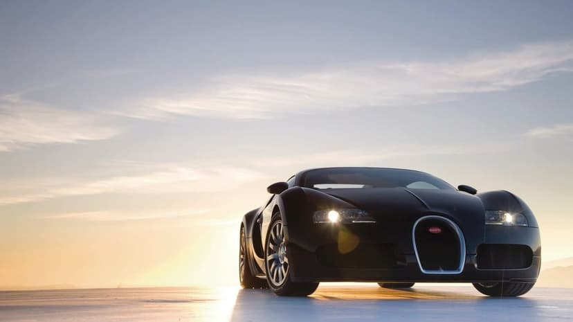 Front view of a black Bugatti Veyron supercar with headlights on against a soft blue and gold sunset sky.