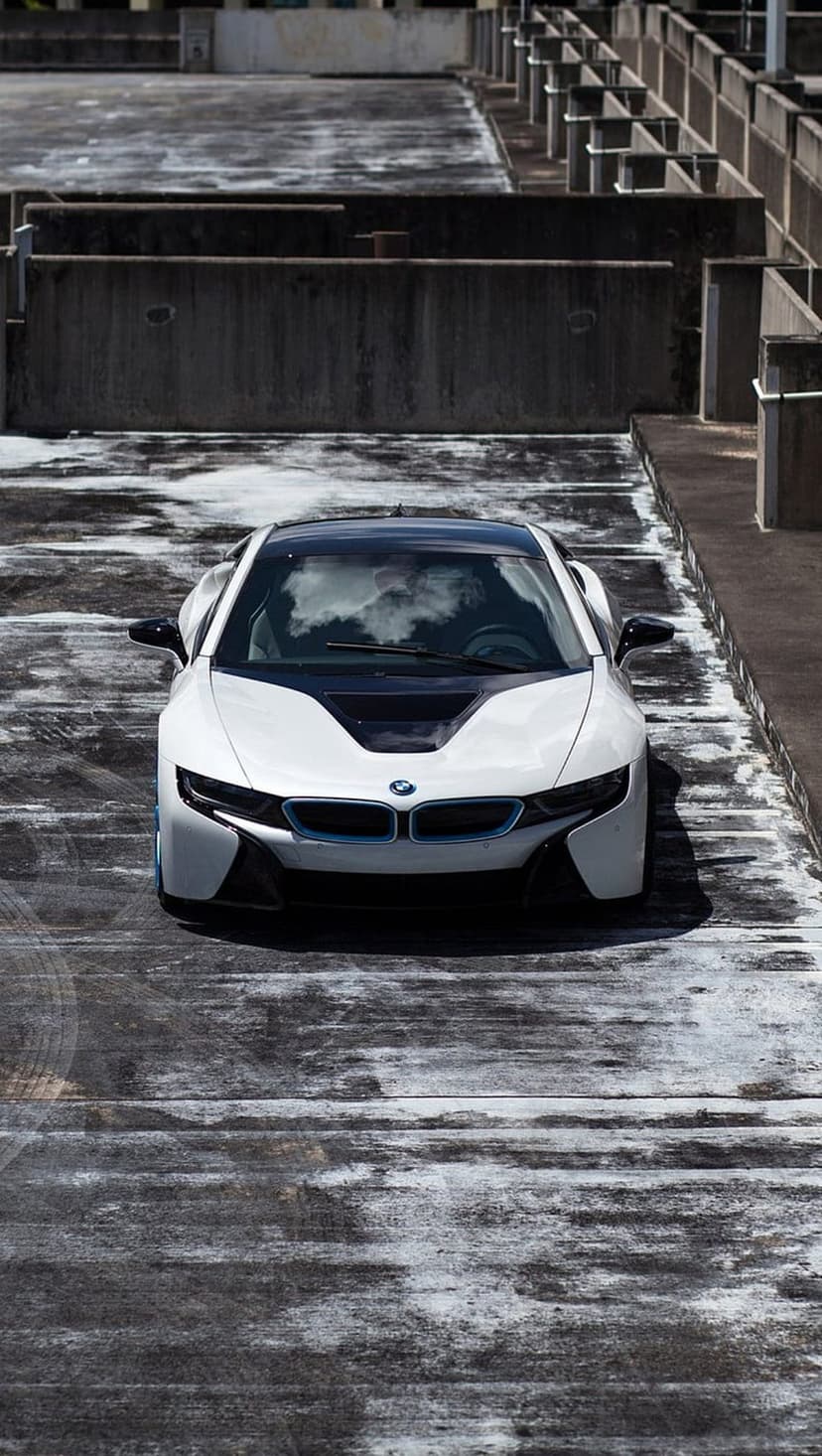White BMW i8 hybrid car on a weathered concrete parking garage rooftop with blue accents and a black roof.