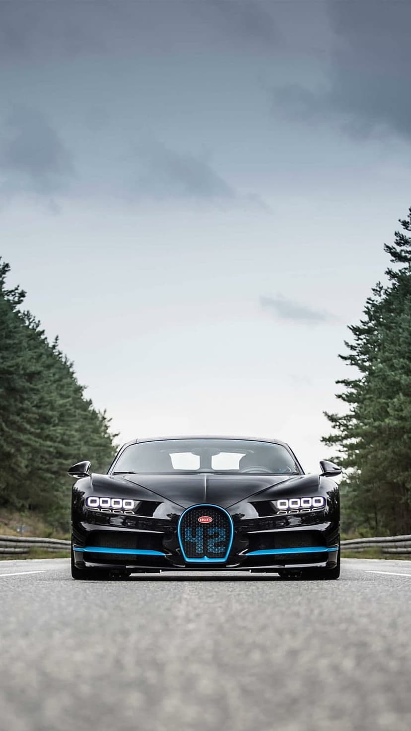 Bugatti Chiron hypercar with blue trim on a paved forest road under a moody grey sky during daytime.