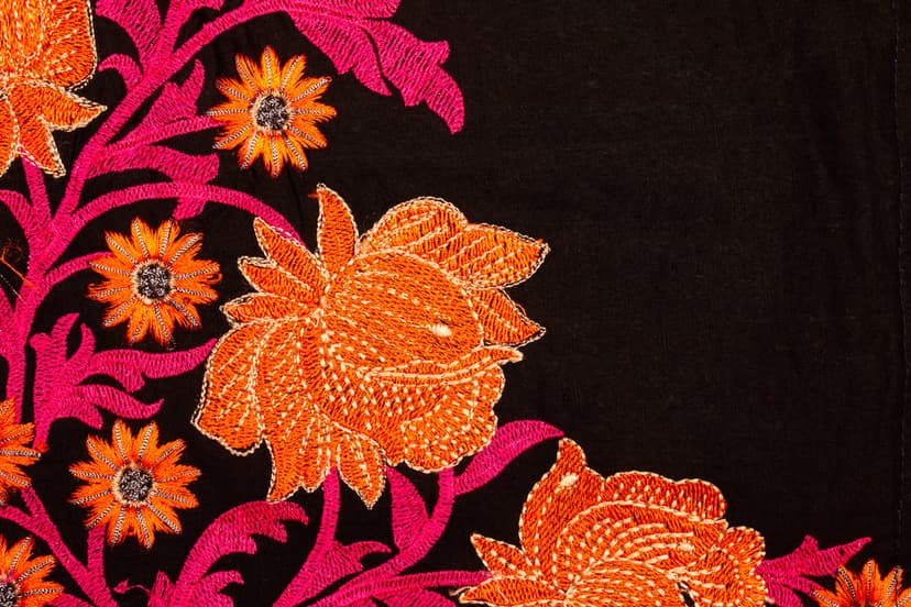 Orange flower embroidery with pink leaves on black fabric featuring detailed thread textures and ornate stitching.