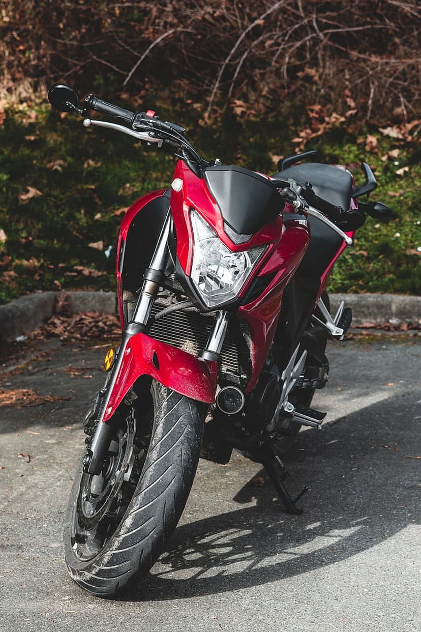 Red motorcycle with chrome accents parked on asphalt with tree shadows, shown from a low front-facing angle.