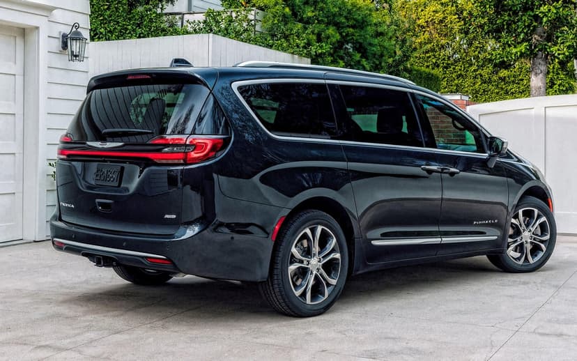 Black Chrysler Pacifica Pinnacle minivan parked in a driveway with white garage and green hedge background.