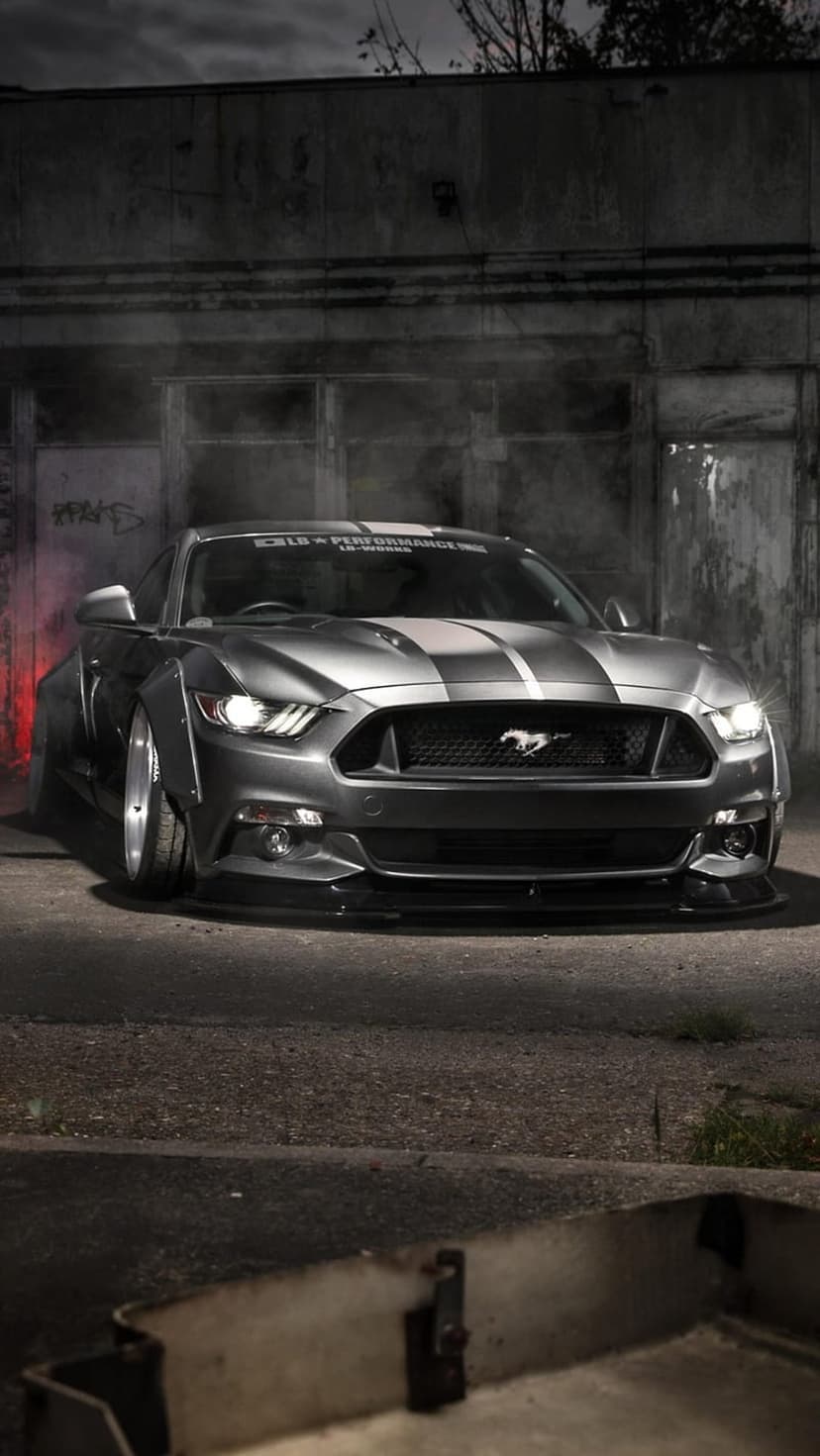Gray Ford Mustang widebody with racing stripes stands in a dark smoky city alley under dramatic low lighting.