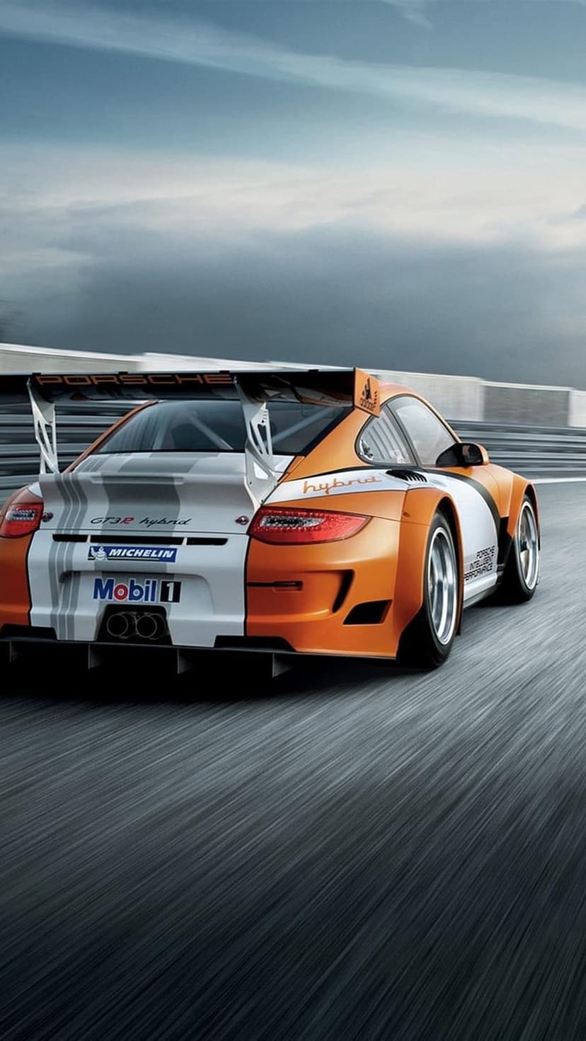 Porsche 911 GT3 R Hybrid race car with orange and white livery speeds on a paved circuit with a large rear wing.