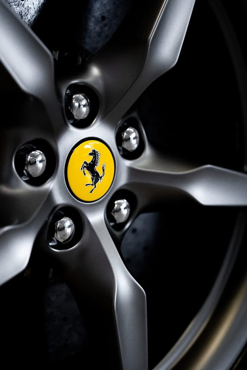 Ferrari prancing horse emblem at the center of a silver alloy wheel with polished lug nuts on a dark background.