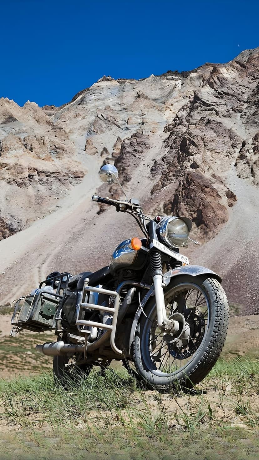 Adventure motorcycle with luggage racks sits on a slope beneath a vast blue sky and rugged desert mountains.