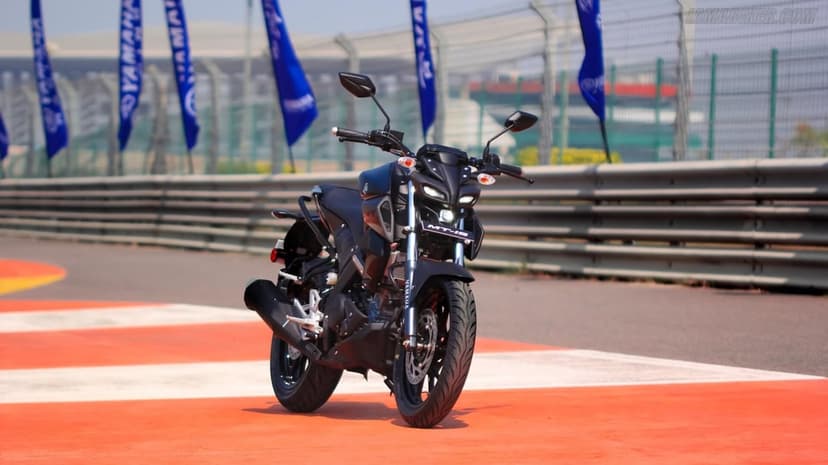 Black Yamaha MT-15 motorcycle parked on a red and orange racetrack curb under bright daylight with blue flags.