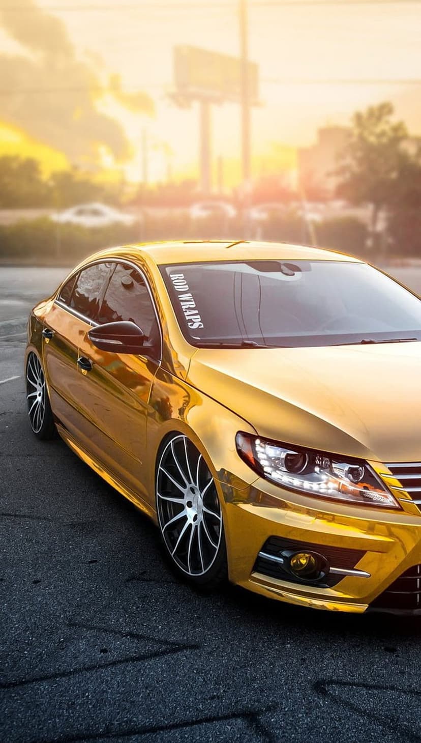 Gold-wrapped Volkswagen CC coupe with black alloy wheels parked during a warm sunset at a low-angle perspective.