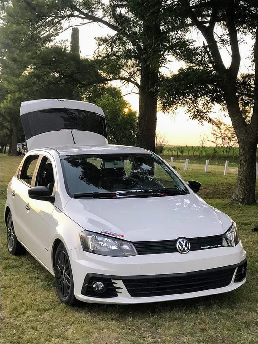 White Volkswagen Golf with an open hatchback parked in a grassy meadow during a golden hour forest sunset.