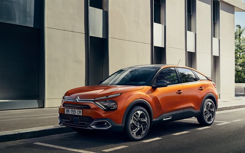 Orange Citroen C4 crossover SUV parked on a city street next to a modern minimalist building in daylight.
