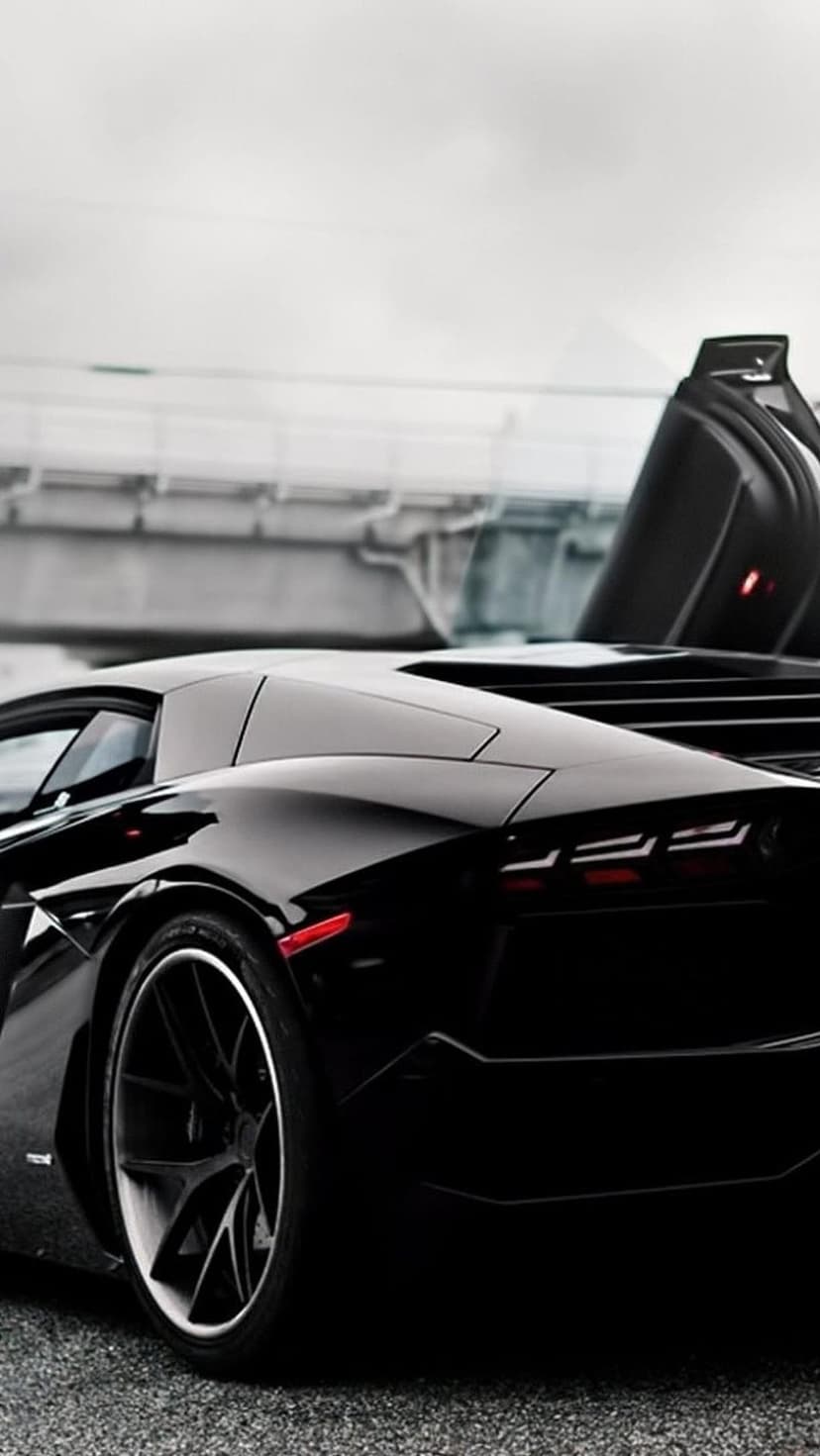 Matte black Lamborghini Aventador rear showing sharp LED lights and wide tires against a blurred gray background.