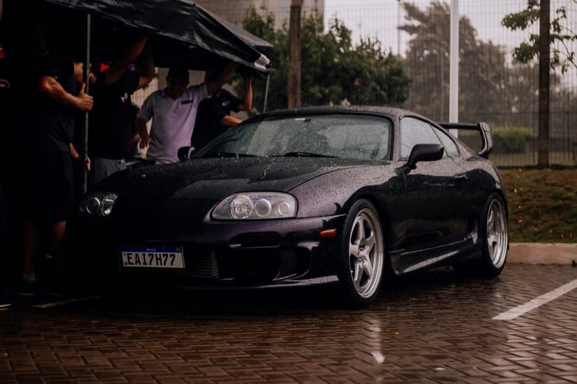 Dark purple Toyota Supra sports car parked on wet cobblestones with visible headlights and license plate EA17H77.