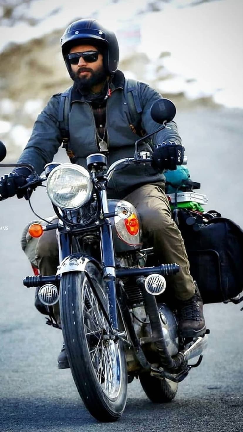 Bearded man wearing a helmet and sunglasses rides a vintage motorcycle through a blurry, rocky mountain pass.
