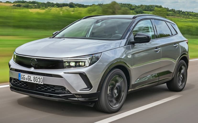 Silver Opel Grandland SUV driving on a road with motion blurred wheels and a green countryside background.