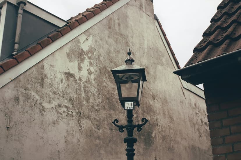 Vintage black street lamp with a warm interior glow mounted on a textured, weathered stone wall in an alley.