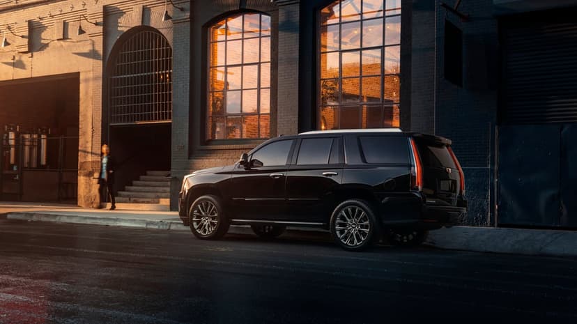 Black luxury SUV parked on a city street in front of a dark building with golden sunset reflections in the windows.