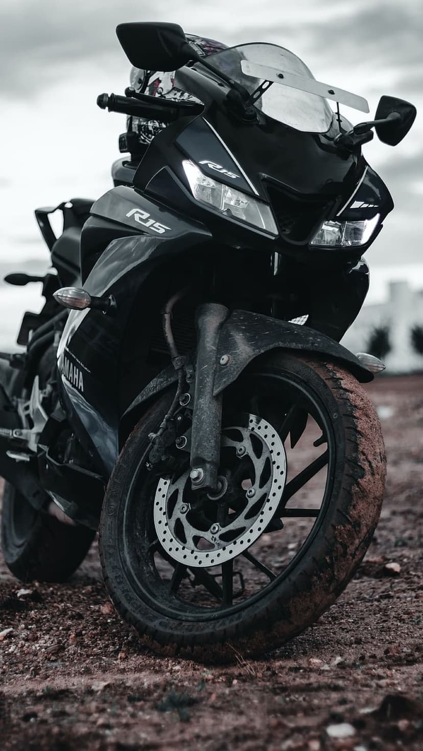 Yamaha R15 front wheel and brake disc on a gravel surface beneath a cloudy sky in a low-angle vertical shot.