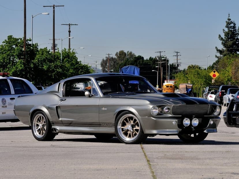 Silver Shelby GT500 Eleanor muscle car with black stripes and chrome wheels parked on a sunny paved lot.