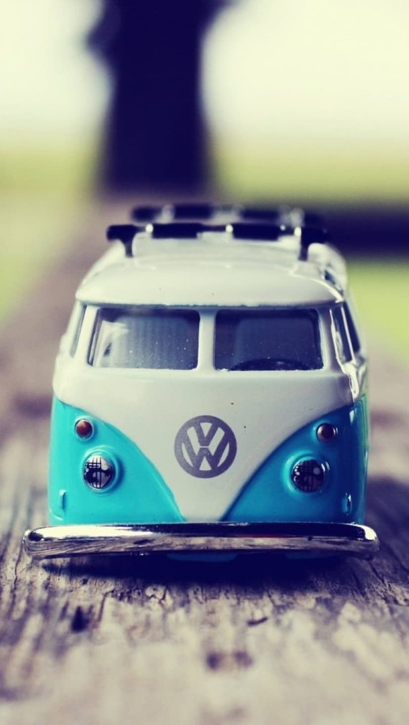 Turquoise and white toy VW bus on a rustic wooden plank with a soft green bokeh background in a macro shot.
