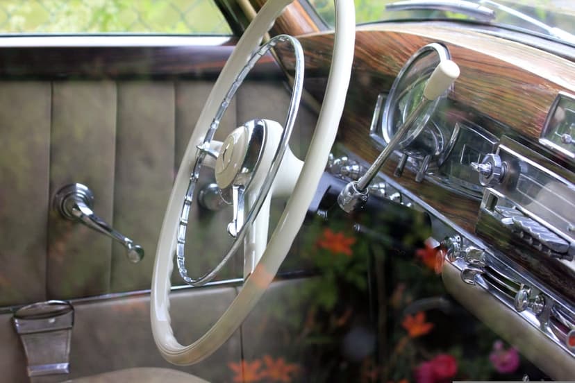 Ivory steering wheel and wood-paneled dashboard with chrome accents inside a restored vintage automobile cabin.