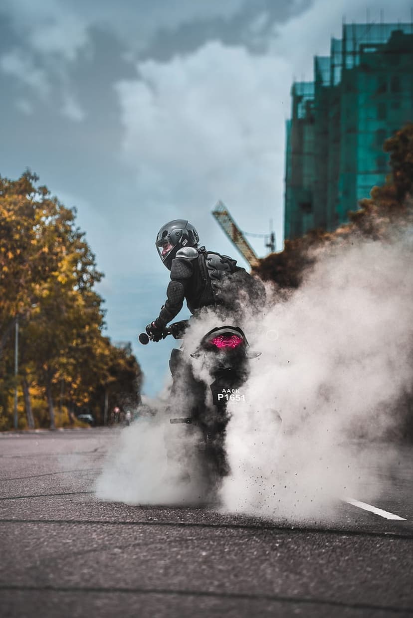Motorcyclist in full gear creates thick white smoke during a burnout on an urban street near a construction site.